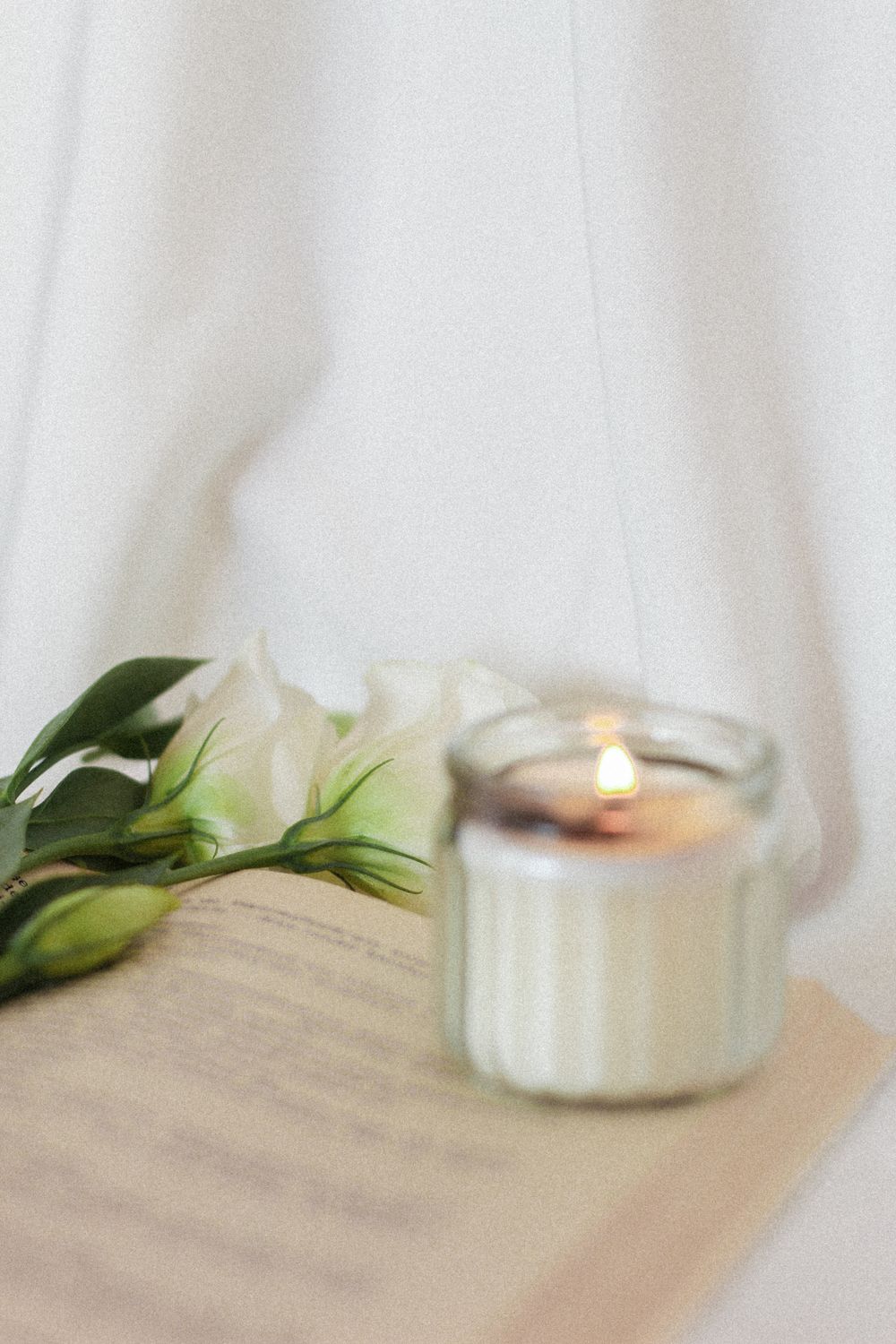 A lit candle and white flowers resting on an open book